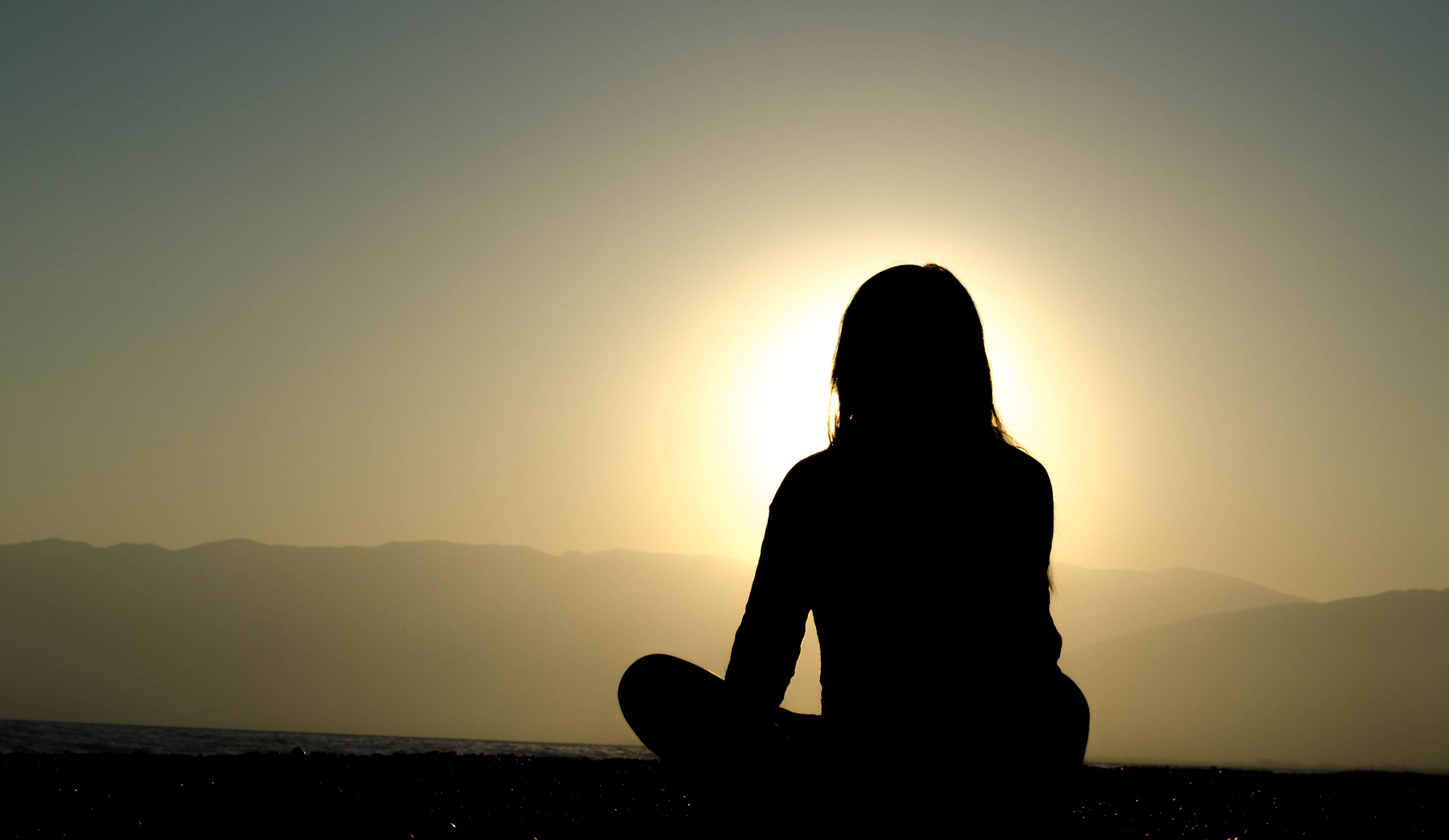 Woman silhouetted by the sun as she meditates