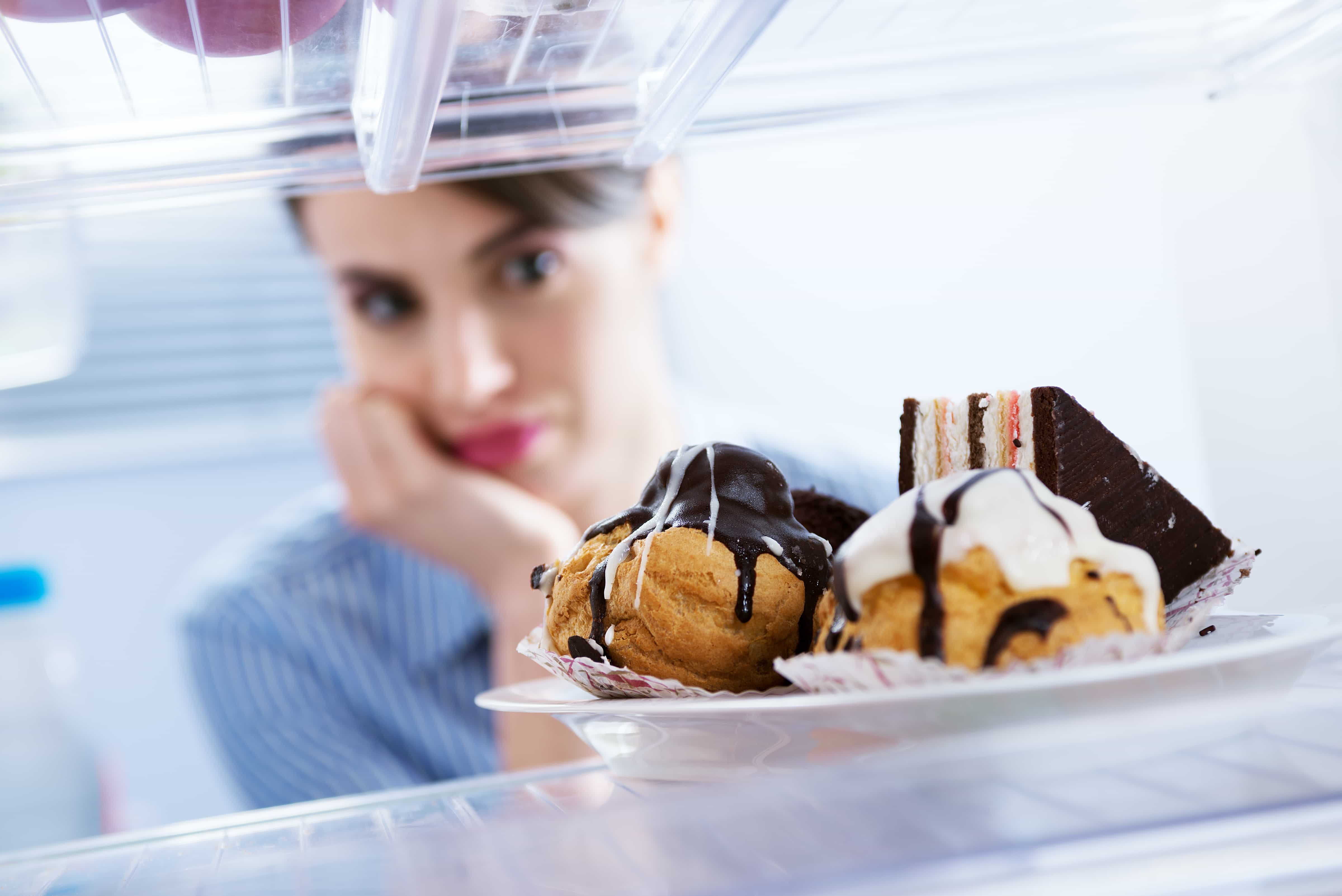 Hungry woman in front of refrigerator craving chocolate pastries